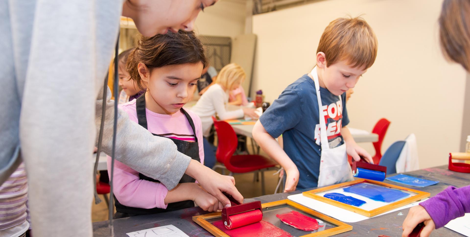 A woman wearing a grey sweater is helping kids help roll paint. 