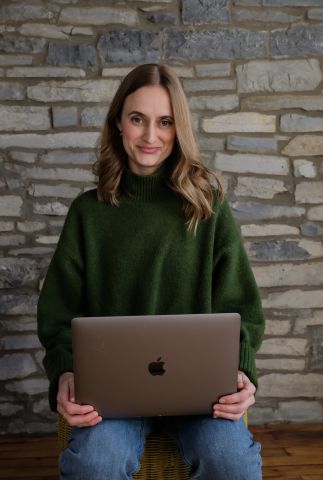 Sophia Fabilli wearing a green sweater and holding a laptop.