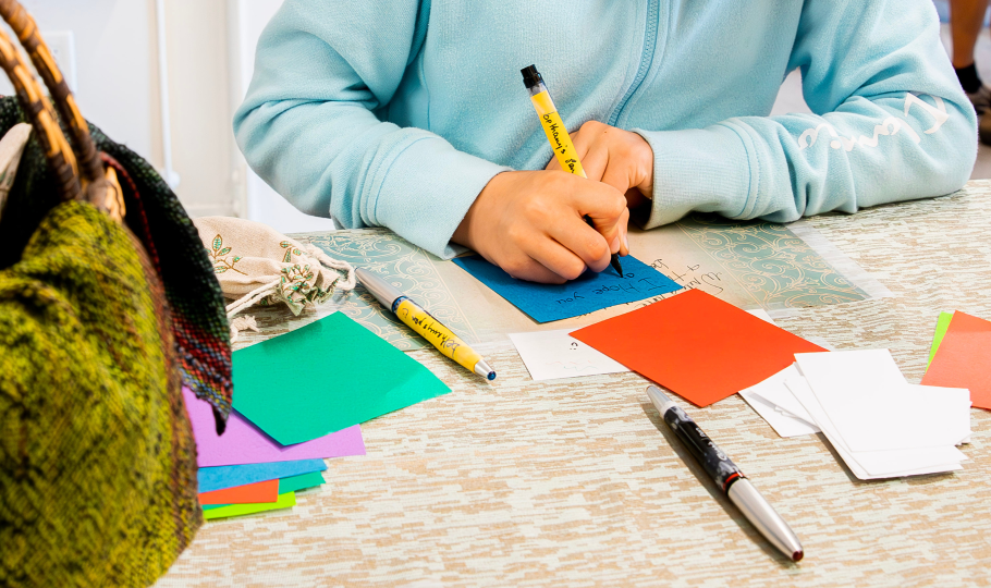 A person's hands writing on pieces of colourful paper.