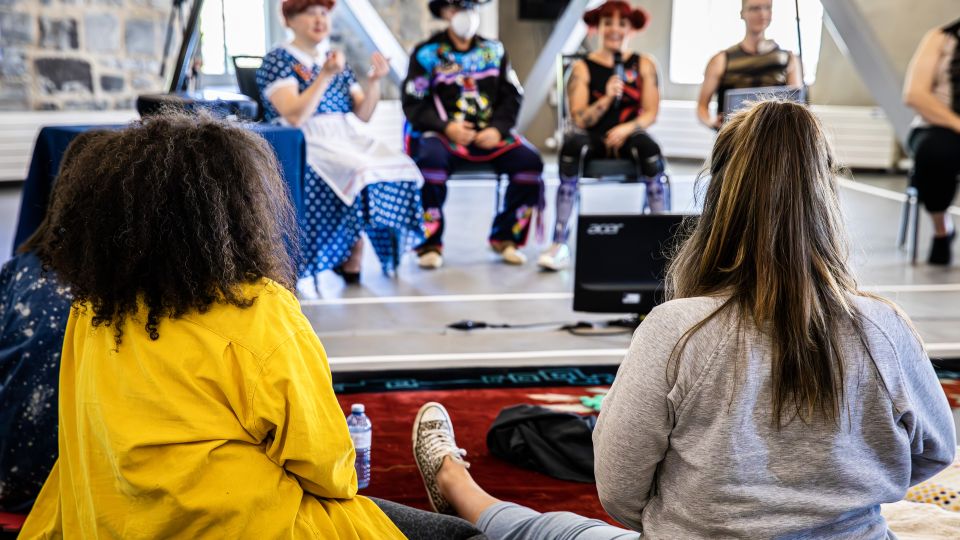 Two people sit on the floor watching a panel discussion. 