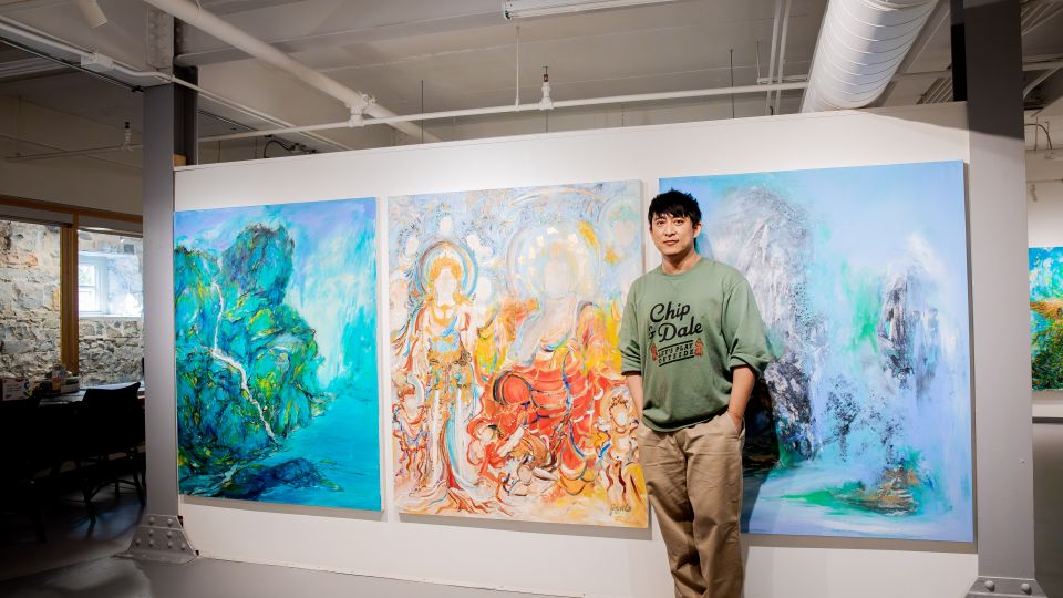 Creativity Studio Artist Pengyuan Wang in front of three large, colourful paintings