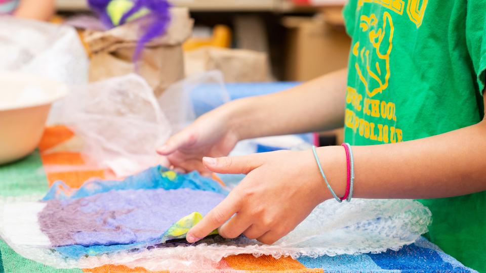 Two hands place coloured paper over bubble wrap. 