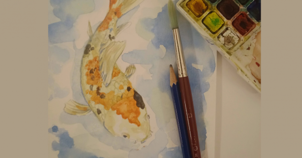 A watercolour painting of a a koi fish, alongside a pencil, paintbrush, and set of watercolour paints.