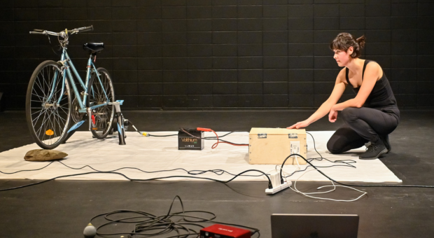  A woman squats down and connects sound cables to a bicycle. 